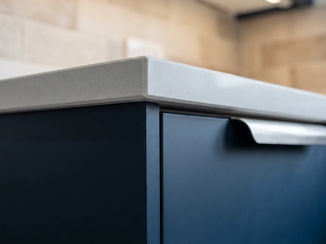 Placeholder image: the mitred edge of a pale quartz worktop meeting a dark blue kitchen cabinet.