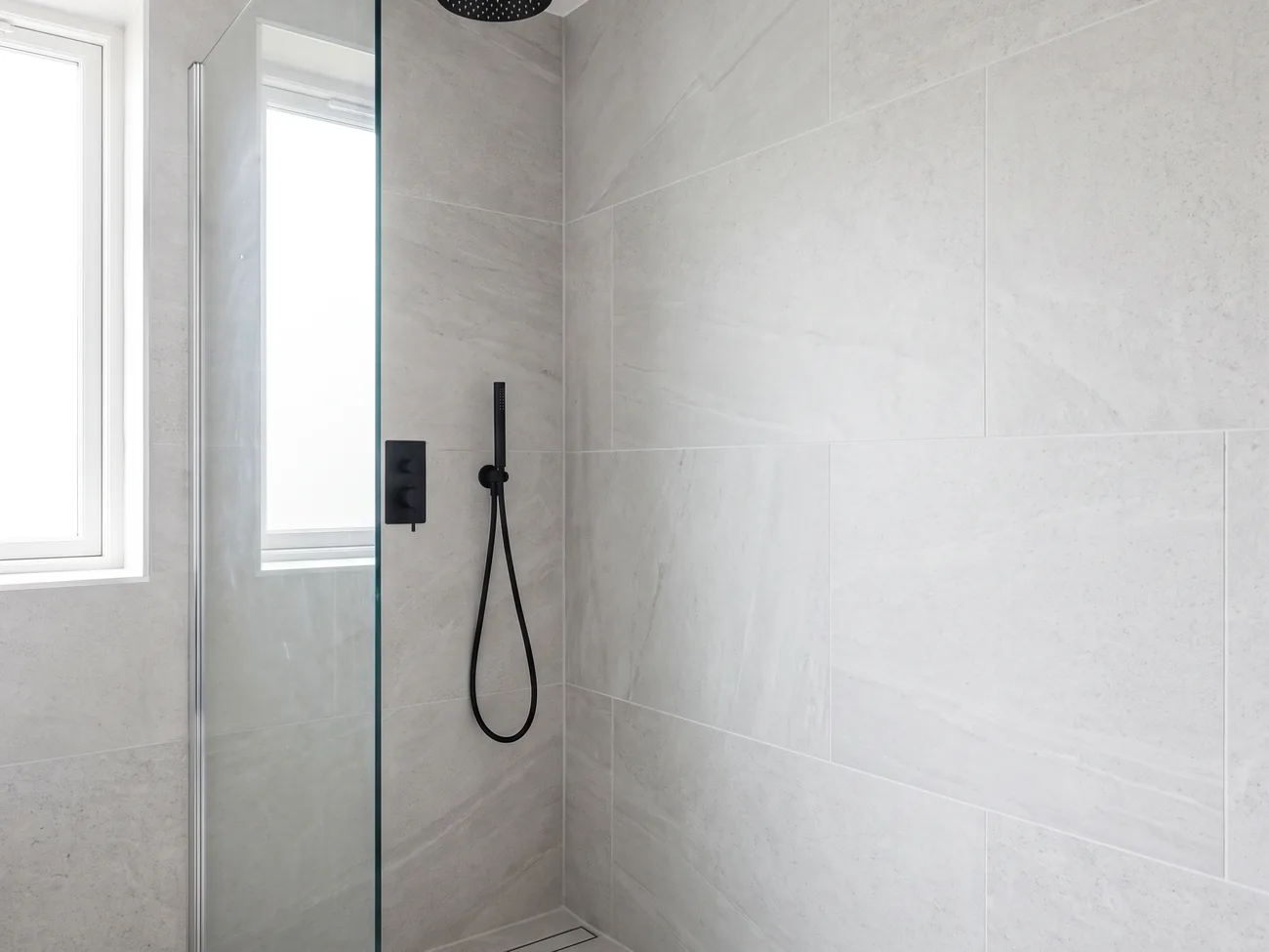 Placeholder image: a tiled walk-in shower with a matt black rainfall head and a glass screen.