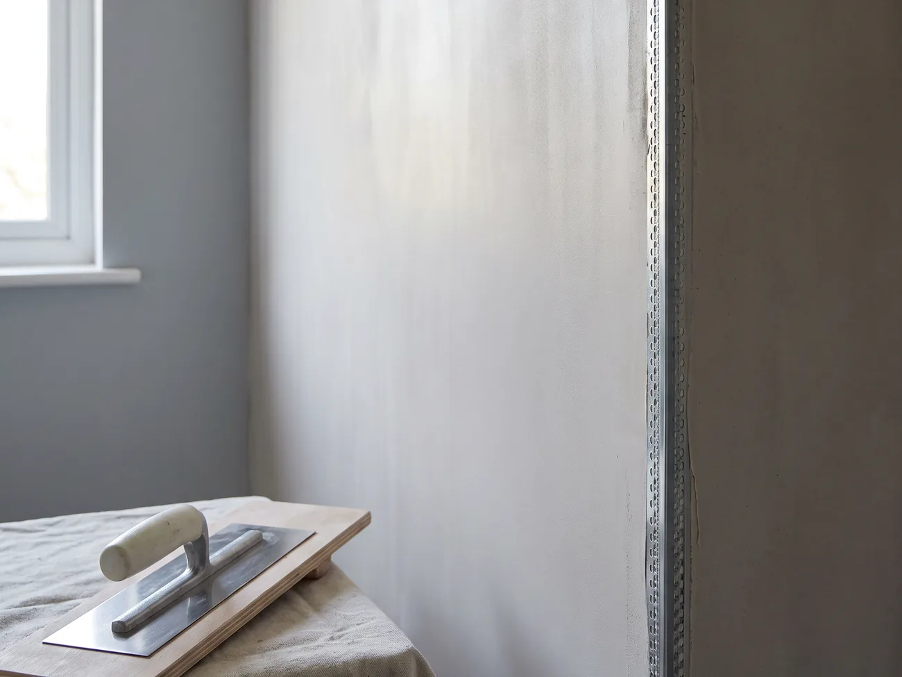 Placeholder image: a freshly skimmed plaster wall with a clean trowel resting on a board.